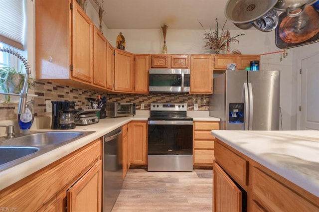 kitchen featuring light wood finished floors, a toaster, stainless steel appliances, light countertops, and tasteful backsplash