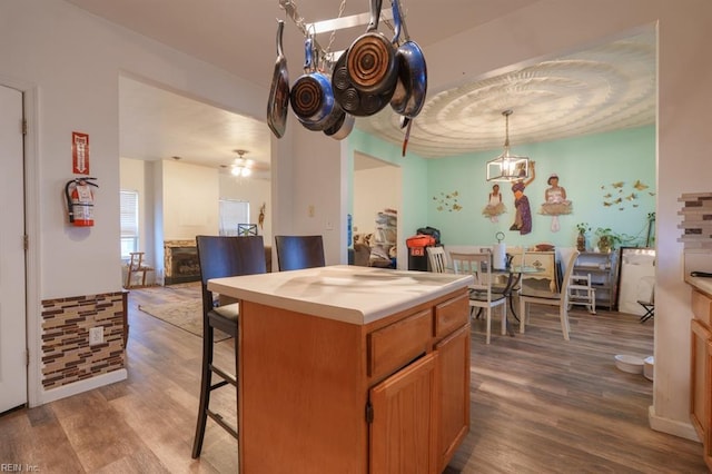 kitchen featuring a breakfast bar area, wood finished floors, a kitchen island, hanging light fixtures, and light countertops