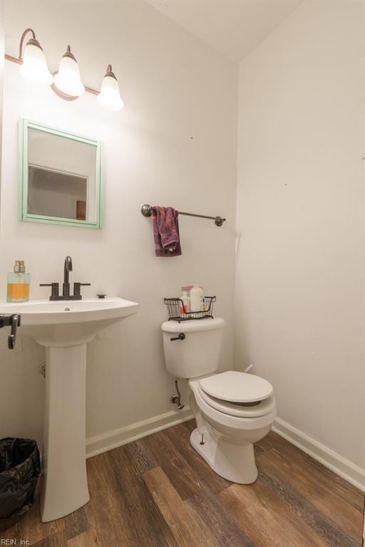 half bath with toilet, wood finished floors, baseboards, and a sink