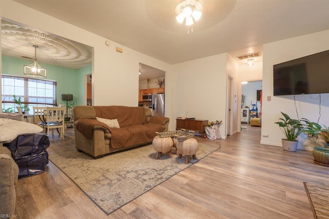 living room with ceiling fan with notable chandelier, wood finished floors, visible vents, and baseboards