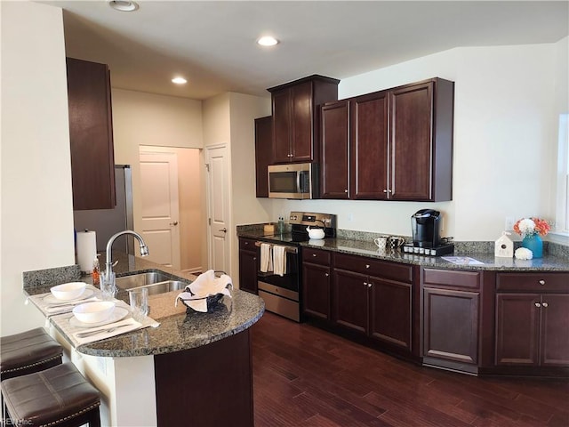 kitchen featuring dark wood-type flooring, a kitchen bar, dark stone countertops, appliances with stainless steel finishes, and a sink