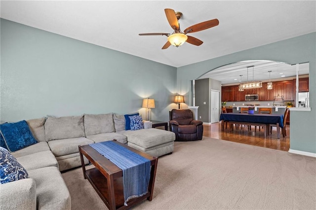 carpeted living room featuring arched walkways, baseboards, and a ceiling fan