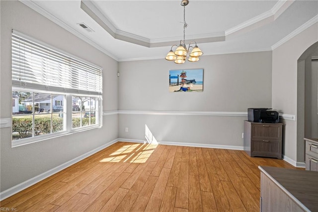 interior space with a tray ceiling, ornamental molding, light wood-style flooring, an inviting chandelier, and arched walkways