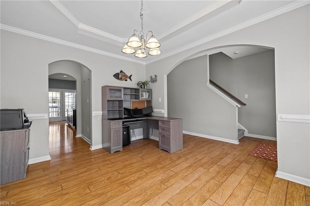 interior space featuring light wood-type flooring, a notable chandelier, baseboards, arched walkways, and a raised ceiling