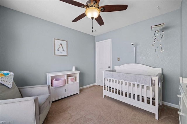 carpeted bedroom with baseboards, a nursery area, and a ceiling fan