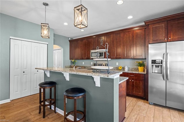 kitchen featuring light stone counters, appliances with stainless steel finishes, light wood-style floors, and a kitchen island with sink