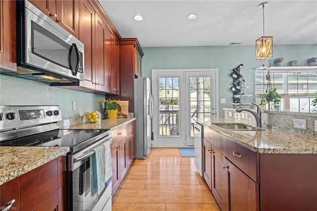 kitchen with light stone counters, a sink, appliances with stainless steel finishes, pendant lighting, and light wood-type flooring