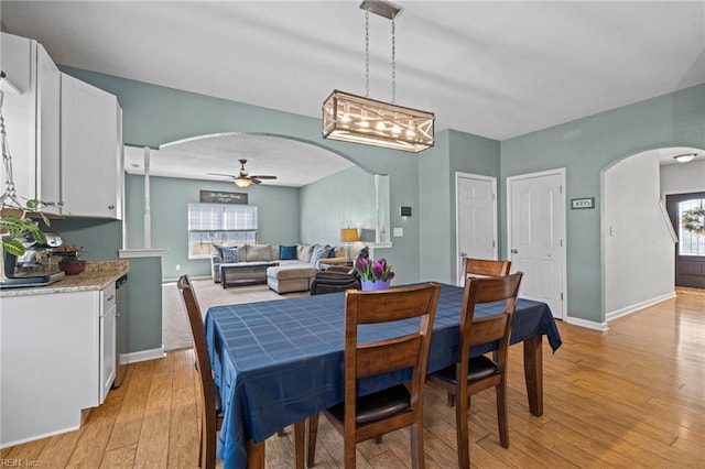 dining room with light wood-style flooring, baseboards, arched walkways, and ceiling fan