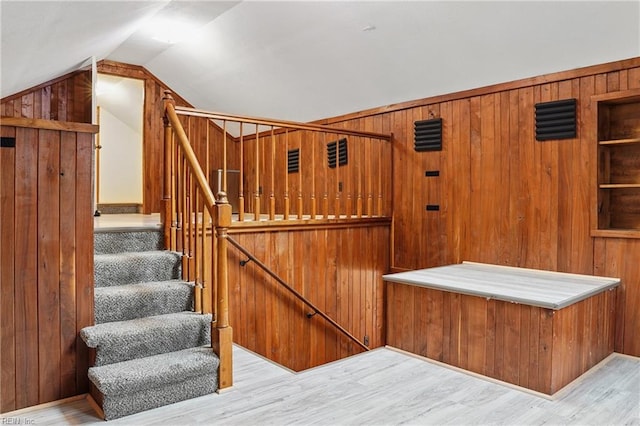 staircase with wooden walls, lofted ceiling, and wood finished floors