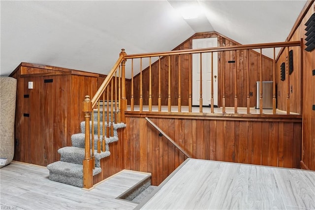 stairway with wood finished floors, wood walls, and vaulted ceiling