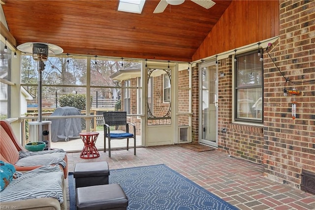 unfurnished sunroom featuring lofted ceiling with skylight, wooden ceiling, and a ceiling fan