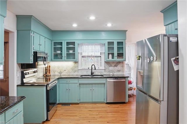 kitchen with decorative backsplash, a sink, stainless steel appliances, light wood finished floors, and glass insert cabinets