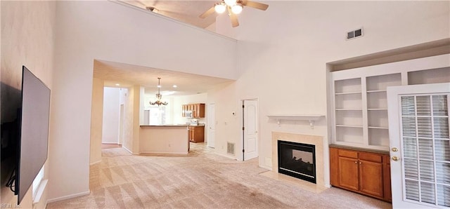 unfurnished living room featuring light colored carpet, a high ceiling, a high end fireplace, and ceiling fan with notable chandelier