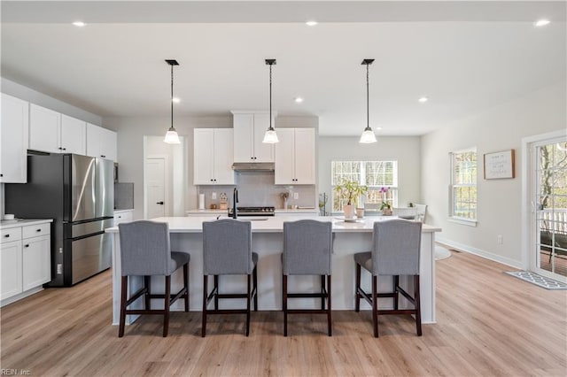 kitchen featuring light countertops, decorative backsplash, freestanding refrigerator, white cabinets, and a kitchen island with sink