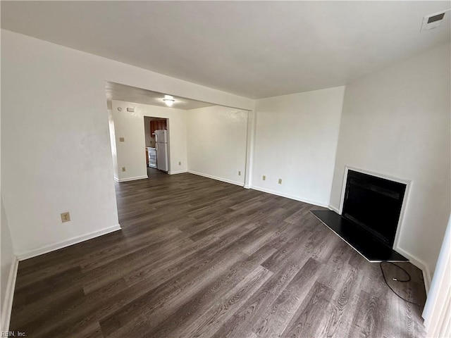 unfurnished living room with dark wood-style floors, visible vents, a fireplace with raised hearth, and baseboards