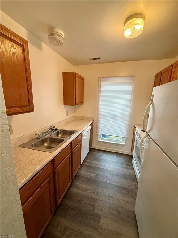 kitchen with white appliances, brown cabinetry, visible vents, dark wood finished floors, and a sink