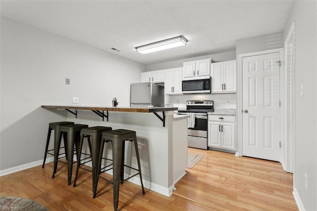 kitchen with a kitchen breakfast bar, stainless steel appliances, a peninsula, light wood-style floors, and white cabinetry