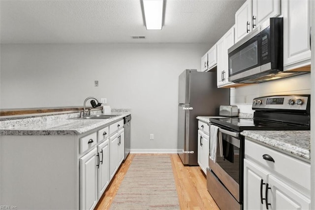 kitchen featuring visible vents, light wood finished floors, a sink, white cabinets, and appliances with stainless steel finishes