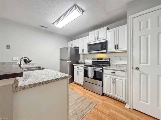 kitchen featuring visible vents, a peninsula, a sink, stainless steel appliances, and light wood-type flooring