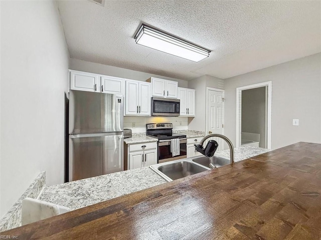 kitchen with a sink, a textured ceiling, white cabinetry, and stainless steel appliances