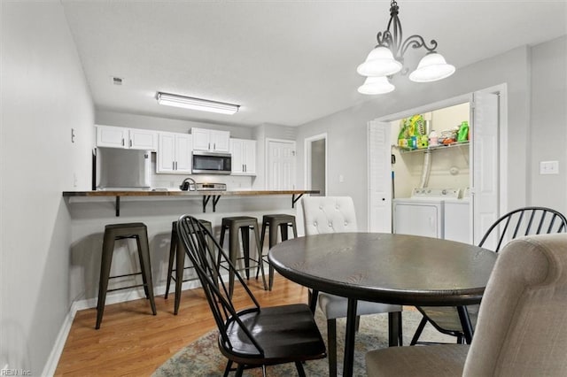 dining room featuring visible vents, baseboards, washer and clothes dryer, light wood-type flooring, and an inviting chandelier