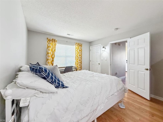 bedroom featuring visible vents, baseboards, light wood-style floors, and a textured ceiling