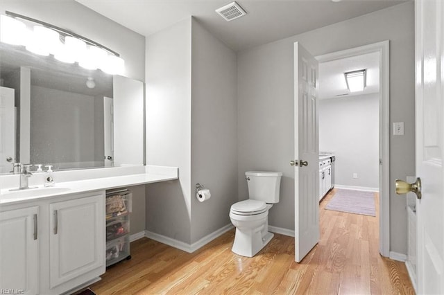 bathroom featuring visible vents, baseboards, toilet, wood finished floors, and vanity