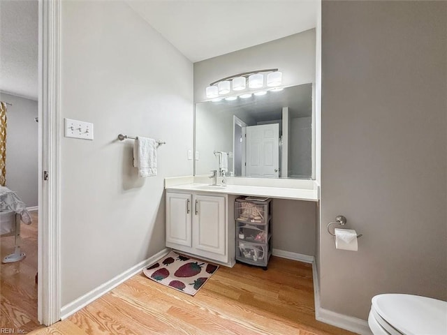 bathroom with toilet, vanity, baseboards, and wood finished floors