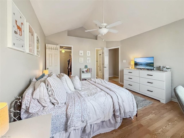 bedroom featuring ceiling fan, vaulted ceiling, a closet, a walk in closet, and light wood-type flooring