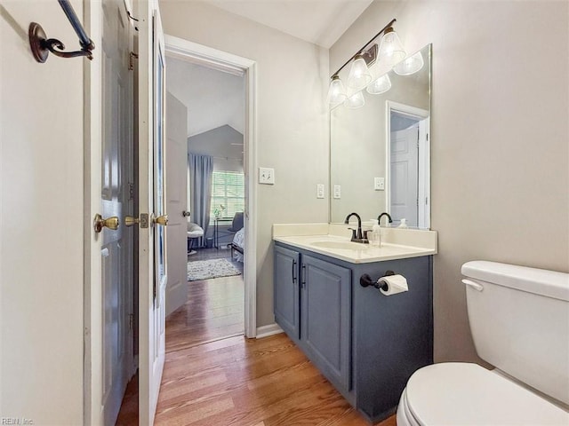 ensuite bathroom featuring connected bathroom, toilet, vanity, and wood finished floors