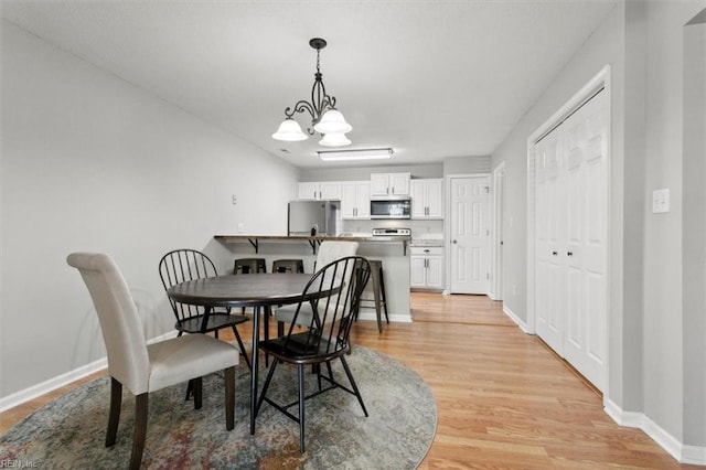 dining room with baseboards, a notable chandelier, and light wood finished floors