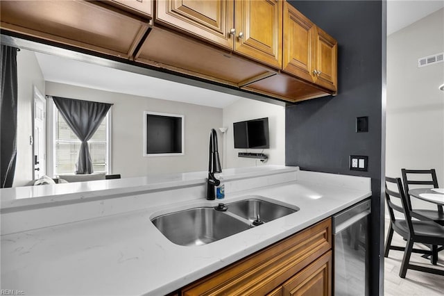 kitchen featuring light stone counters, brown cabinetry, visible vents, a sink, and stainless steel dishwasher