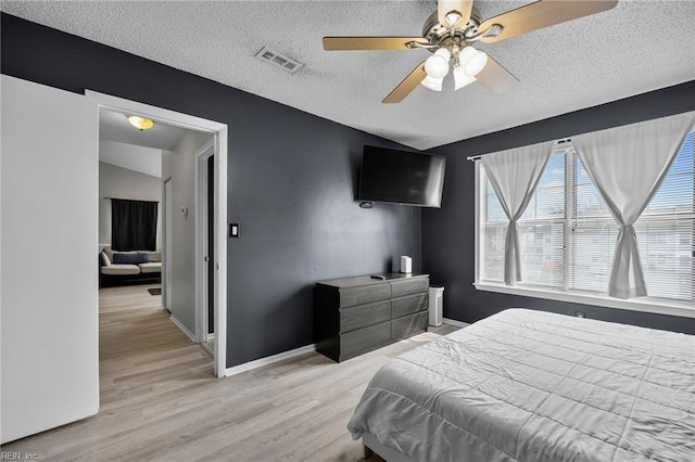 bedroom with a ceiling fan, baseboards, visible vents, light wood finished floors, and a textured ceiling