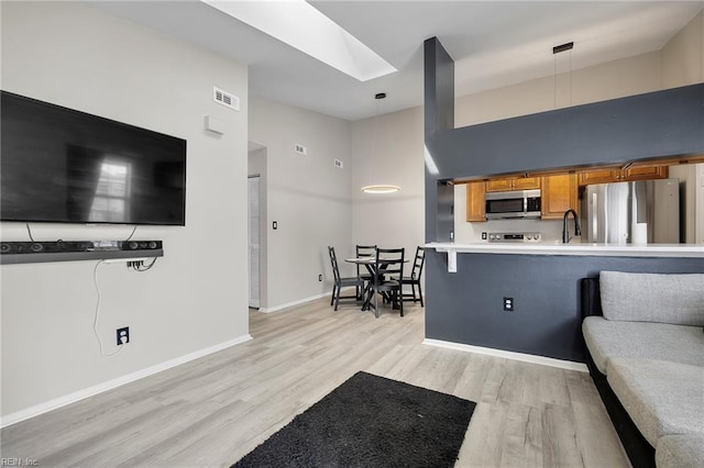 kitchen featuring light wood finished floors, baseboards, light countertops, brown cabinetry, and stainless steel appliances