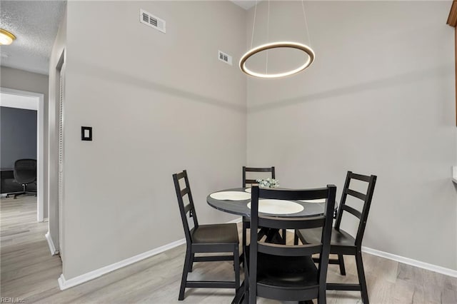 dining space with visible vents, baseboards, a textured ceiling, and wood finished floors