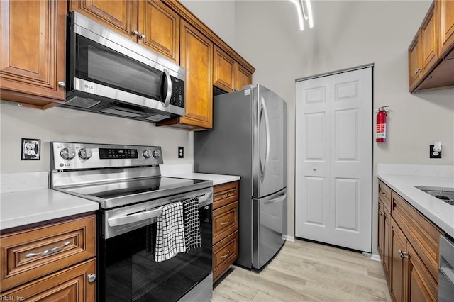 kitchen featuring light wood-type flooring, brown cabinets, stainless steel appliances, arched walkways, and light countertops