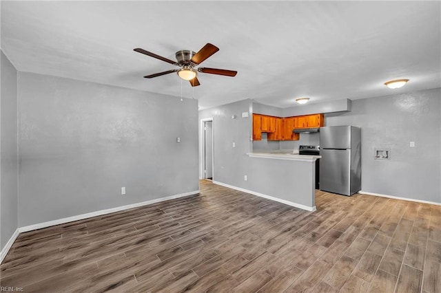 kitchen with a ceiling fan, wood finished floors, freestanding refrigerator, light countertops, and under cabinet range hood