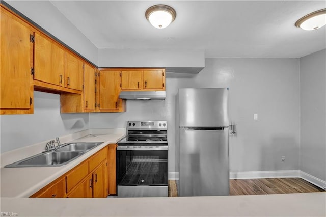 kitchen with under cabinet range hood, brown cabinets, appliances with stainless steel finishes, wood finished floors, and a sink