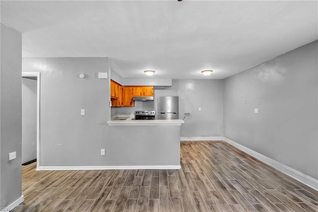 kitchen featuring baseboards, wood finish floors, under cabinet range hood, appliances with stainless steel finishes, and brown cabinets