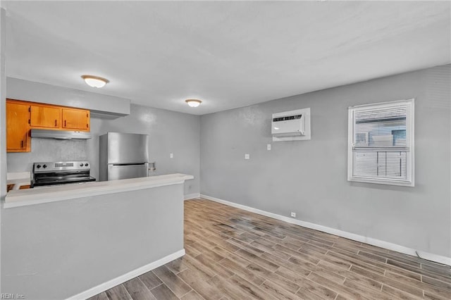 kitchen with baseboards, stainless steel appliances, an AC wall unit, under cabinet range hood, and light wood-type flooring