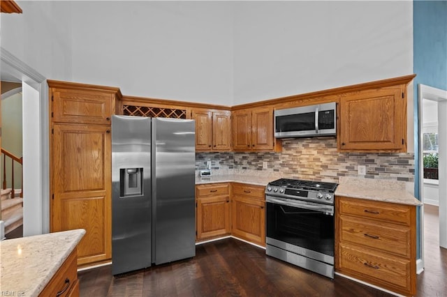 kitchen featuring stainless steel appliances, brown cabinets, a towering ceiling, and decorative backsplash