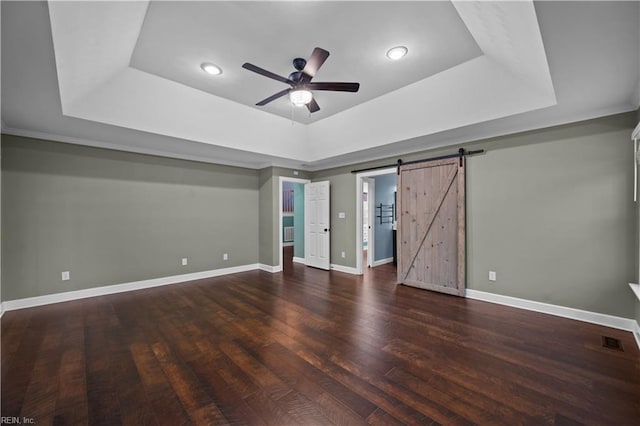 interior space featuring wood finished floors, baseboards, visible vents, a tray ceiling, and a barn door