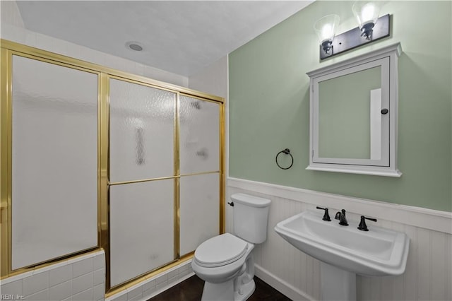 full bath featuring wainscoting, toilet, a shower stall, and a sink