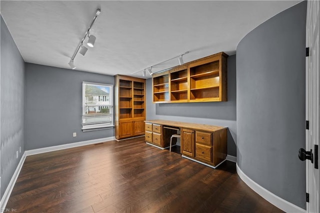 unfurnished office featuring visible vents, track lighting, dark wood-type flooring, baseboards, and built in desk