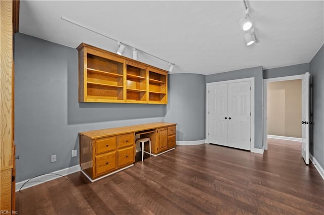 office area with baseboards, built in desk, dark wood finished floors, and rail lighting