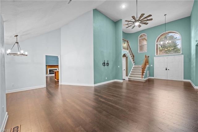 unfurnished living room featuring visible vents, ceiling fan with notable chandelier, wood finished floors, stairway, and baseboards