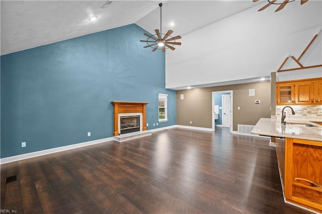 unfurnished living room with visible vents, a sink, ceiling fan, a glass covered fireplace, and dark wood-style flooring