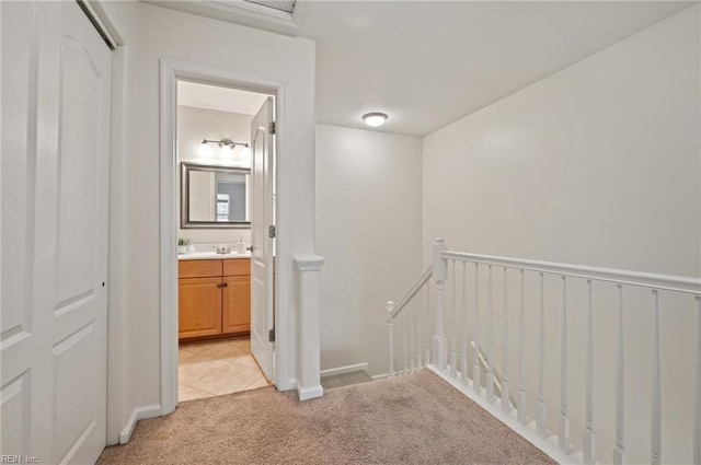 hallway featuring a sink, light tile patterned floors, an upstairs landing, and light carpet