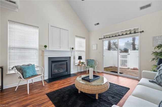 living room featuring visible vents, high vaulted ceiling, a fireplace with flush hearth, and wood finished floors