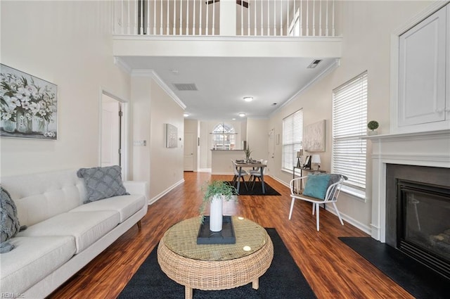 living area with baseboards, ornamental molding, a high ceiling, wood finished floors, and a glass covered fireplace